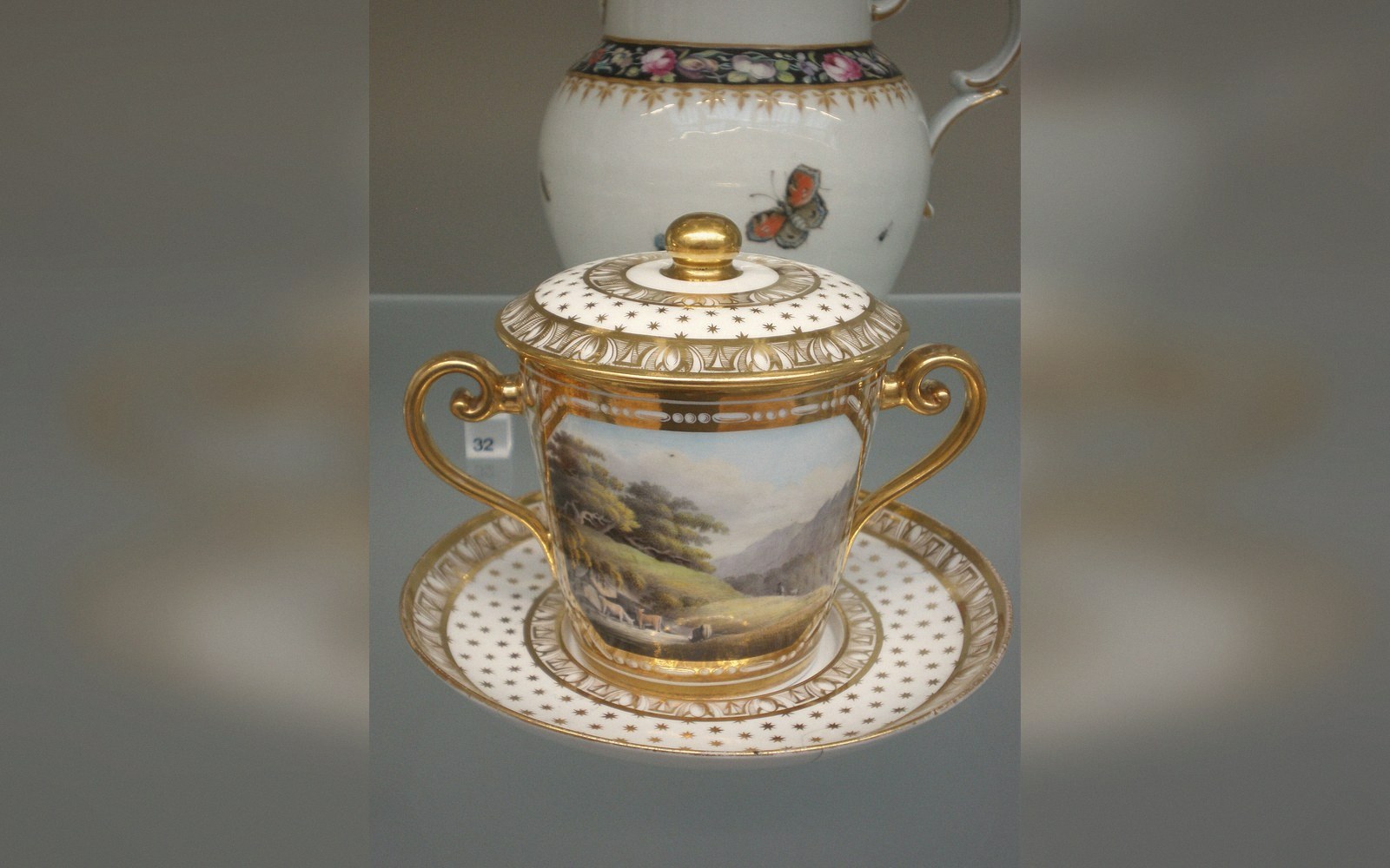 Gilded porcelain lidded cup and saucer with a painted landscape scene