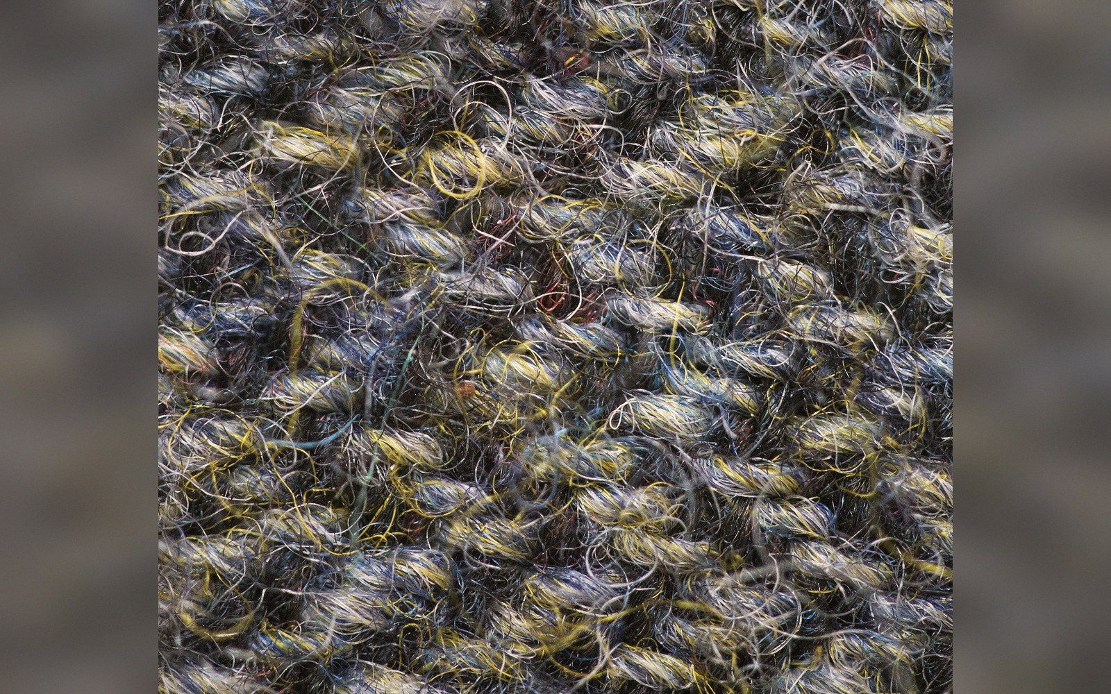 Close-up of looped wool fibers in mottled gray, yellow and blue tweed yarn