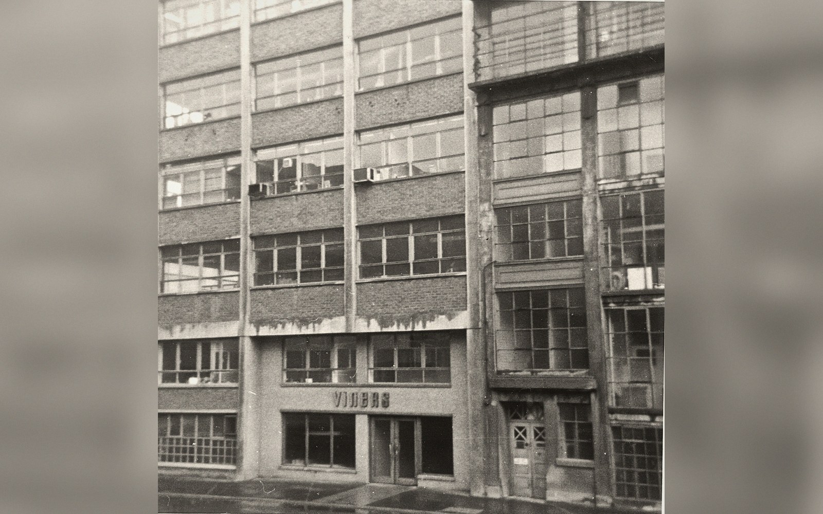 Multi-storey brick factory building with rows of large windows and a ground-floor entrance