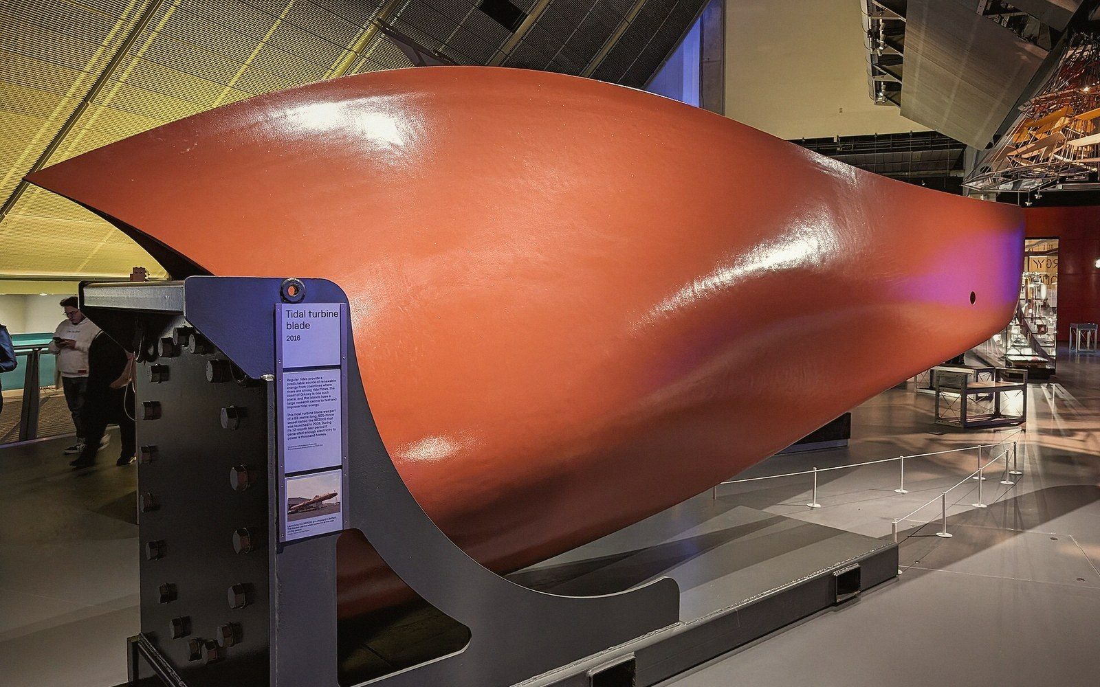 A large orange tidal turbine blade displayed on a museum stand