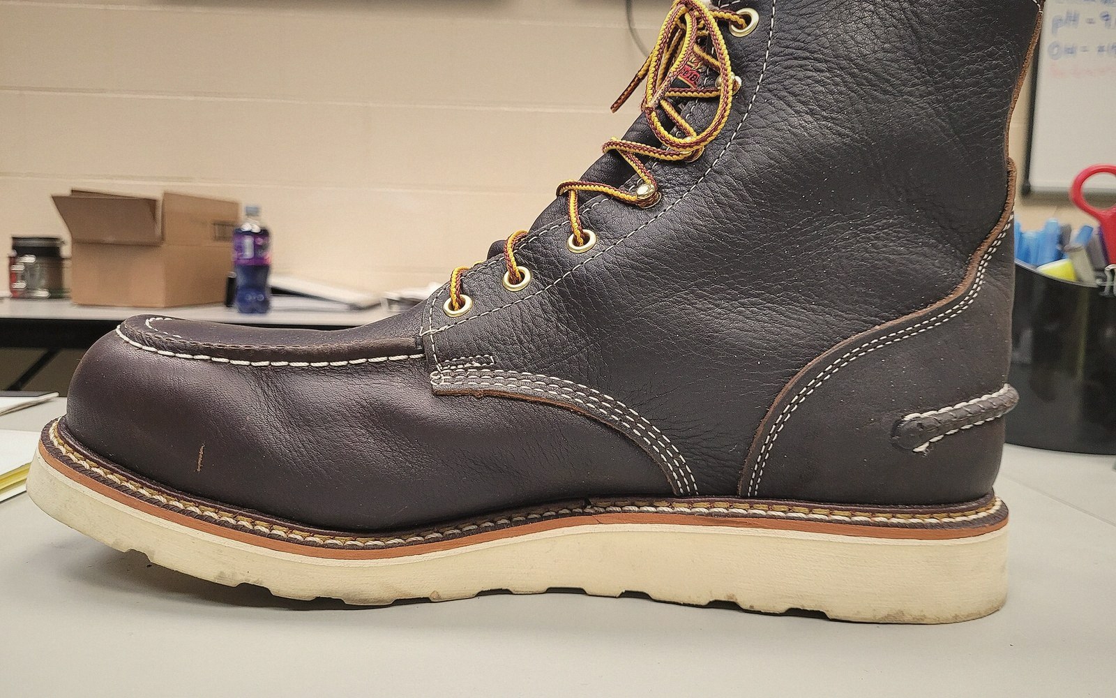 Brown leather work boot with a moc toe and thick white rubber sole on a desk