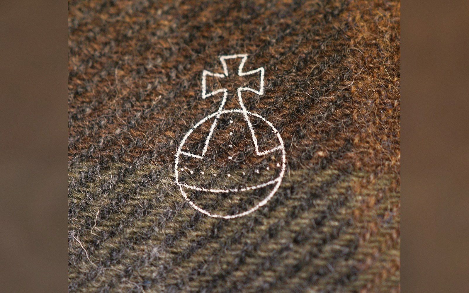 Embroidered orb and cross emblem stitched onto brown herringbone wool fabric